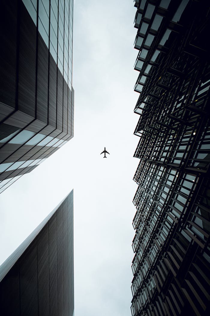 A dramatic view of an airplane flying above modern skyscrapers in London, UK.